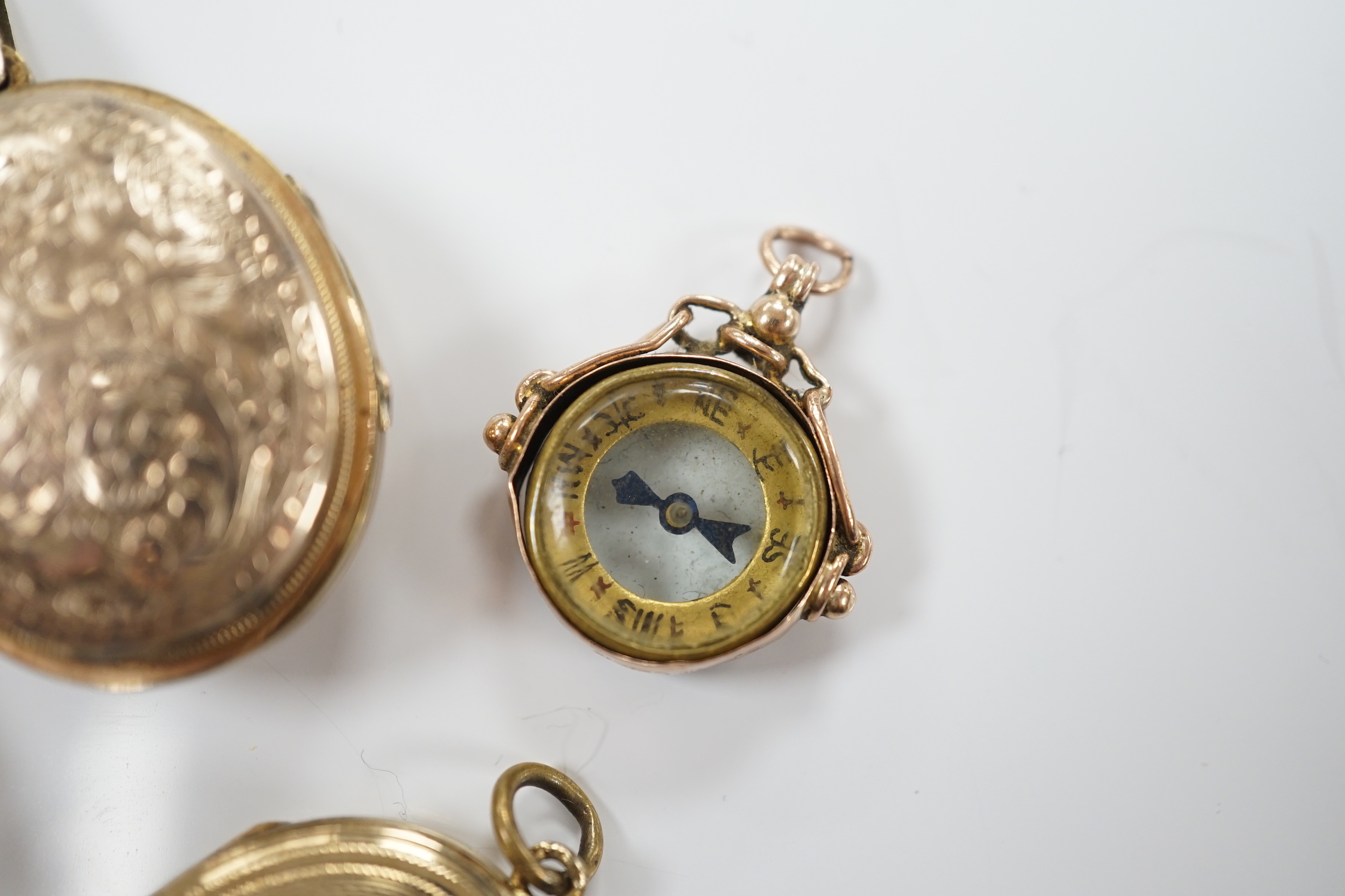 Three assorted early 20th century and later engraved yellow metal overlaid oval lockets including turquoise set, largest 33mm and a 9ct gold mounted compass charm.